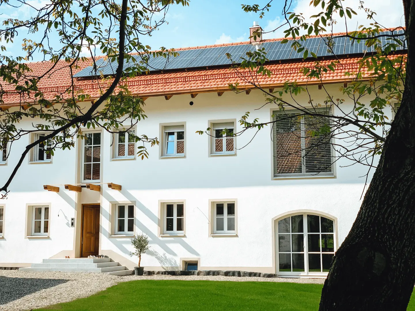 Ein modernes, zweigeschossiges Wohnhaus mit rotem Ziegeldach, Solarzellen und großen Fenstern.