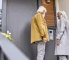 Zwei ältere Personen stehen an einer Eingangstür und betrachten ein Haustelefon oder eine Gegensprechanlage.