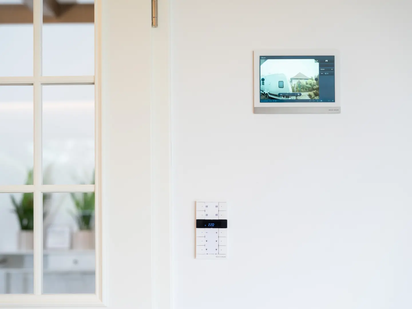 Deckenmonitor mit Kameraansicht und Bedienelementen an der Wand für smarte Heimsteuerung.