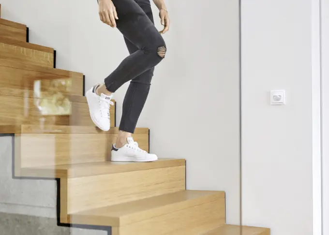 Person in white sneakers descending wooden stairs.