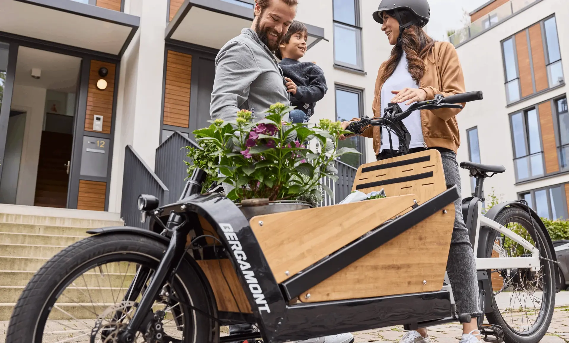 Familie mit einem Lastenrad, das einen Holzkasten mit Pflanzen transportiert, während sie miteinander interagiert.